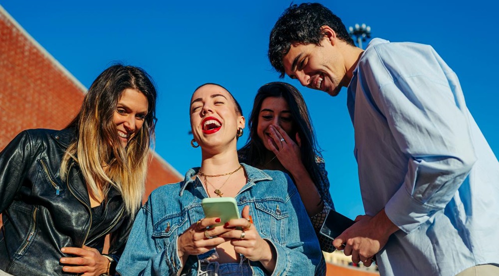 Amigos al aire libre riendo al ver algo en el móvil