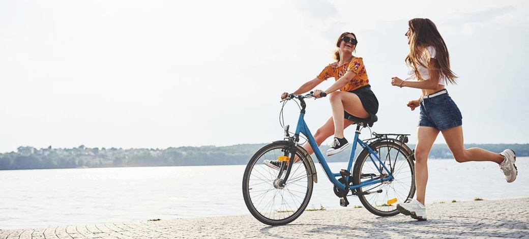 Una mujer en bici y otra corriendo por la playa